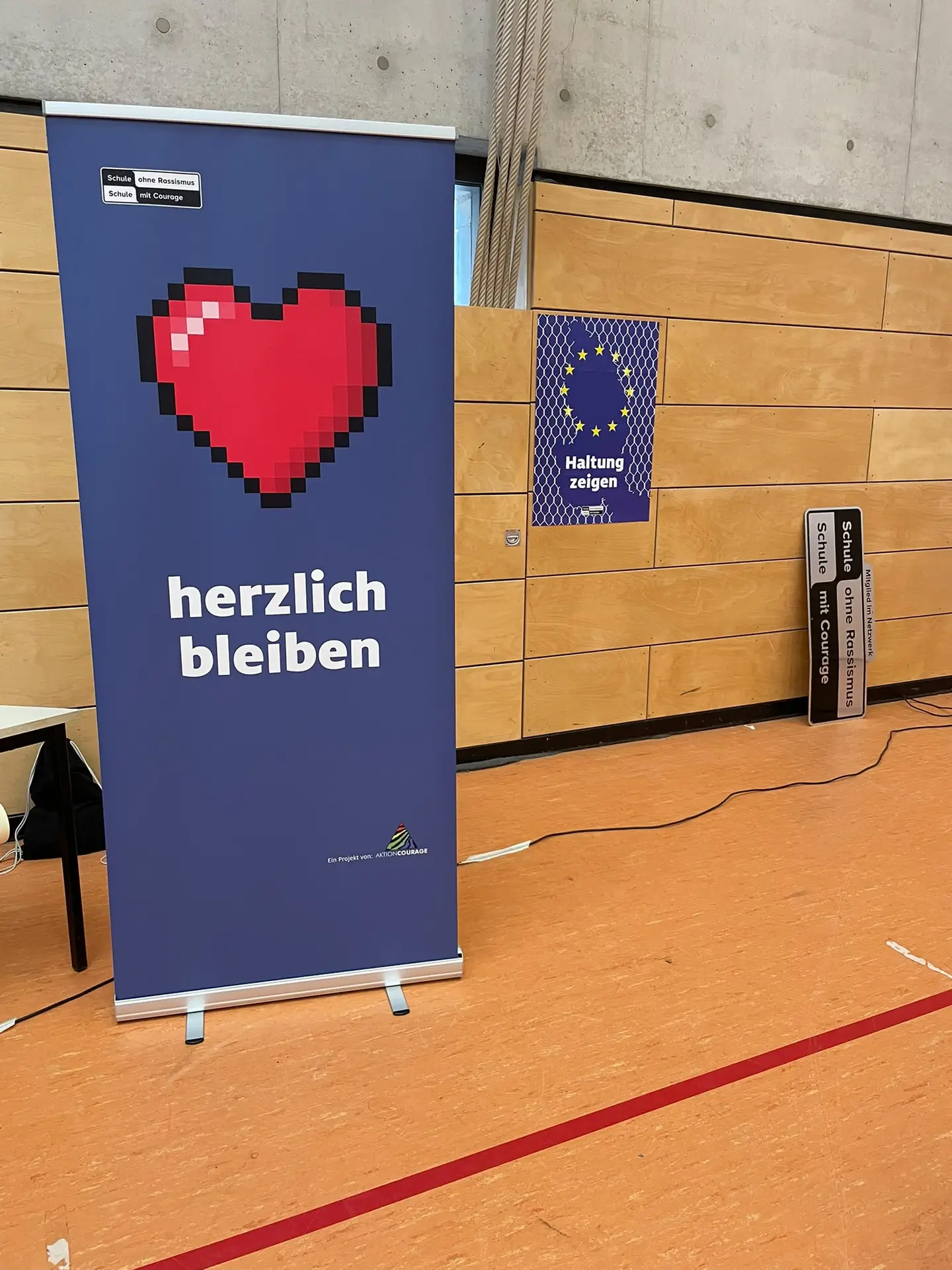 Banner „herzlich bleiben“ und Plakette „Schule ohne Rassismus – Schule mit Courage“